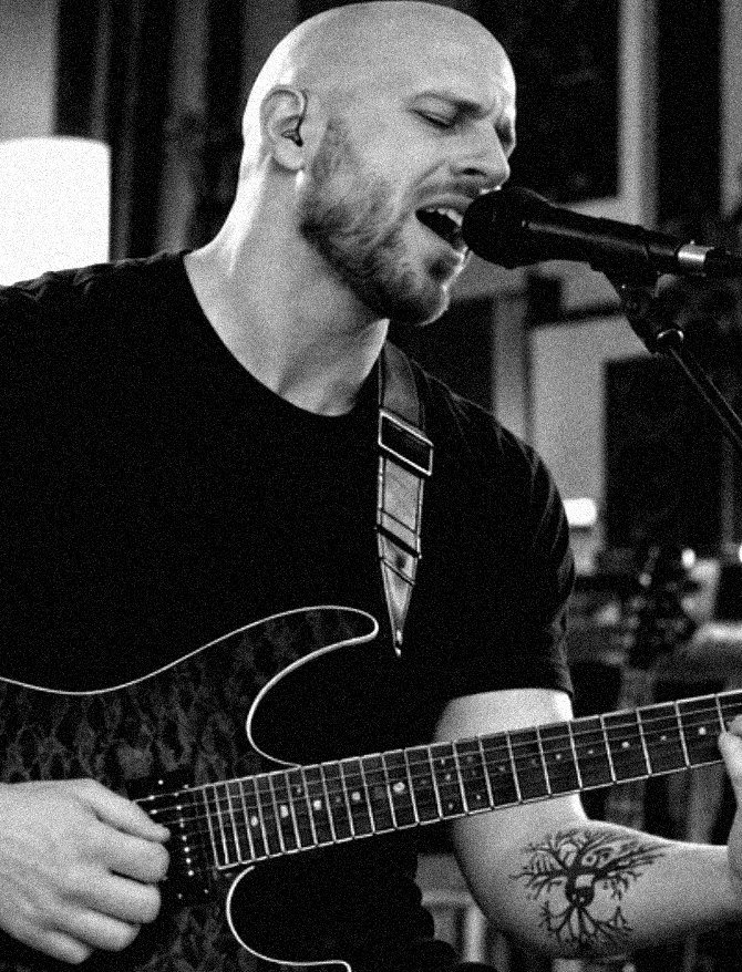 Pete singing into a microphone while playing electric guitar